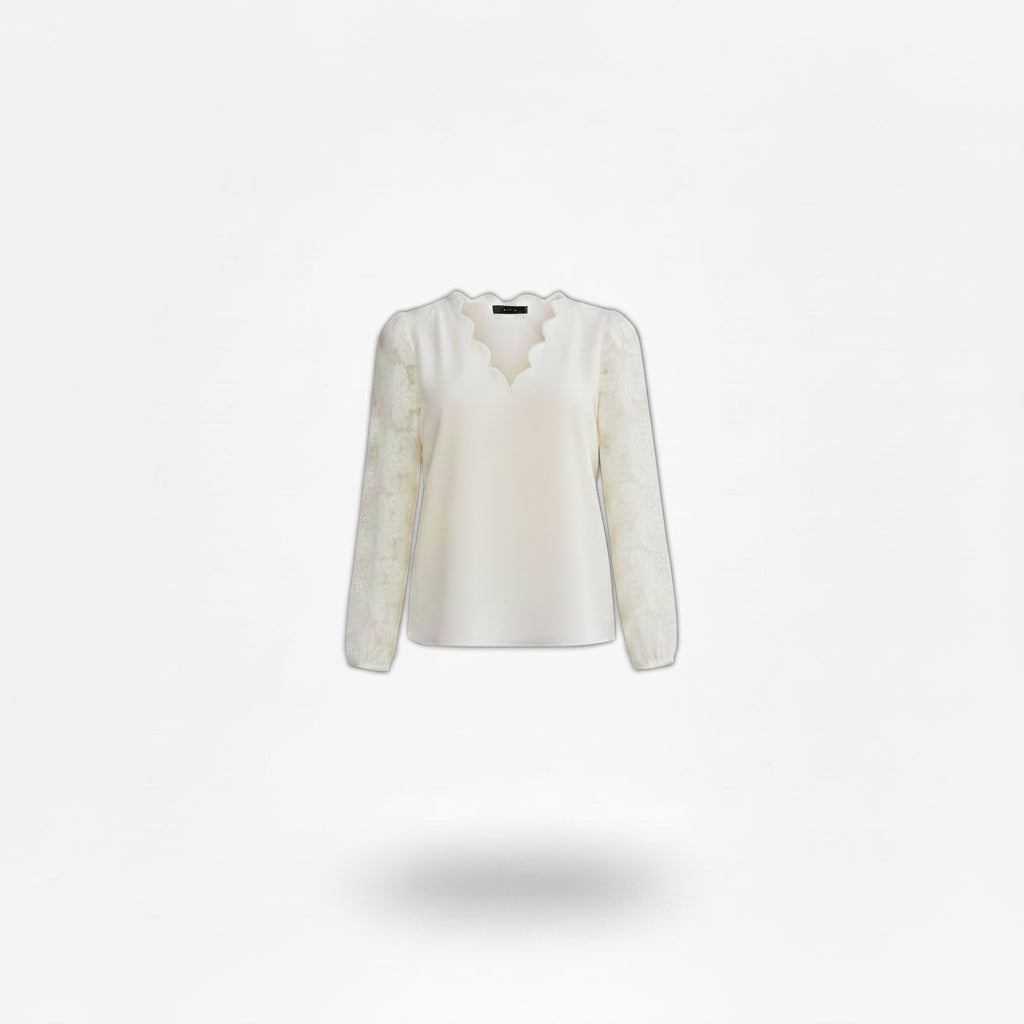 Woman wearing a white lace blouse and black jeans, standing against a neutral background.