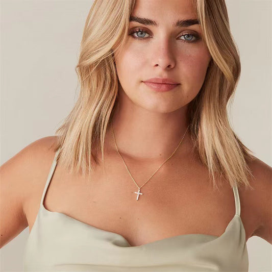 Woman wearing a gold necklace with a cross pendant on a neutral background