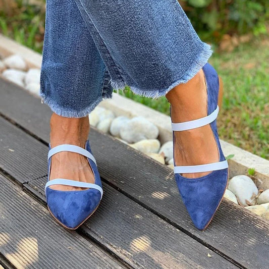 Blue suede shoes with white straps worn with blue jeans on a wooden surface.