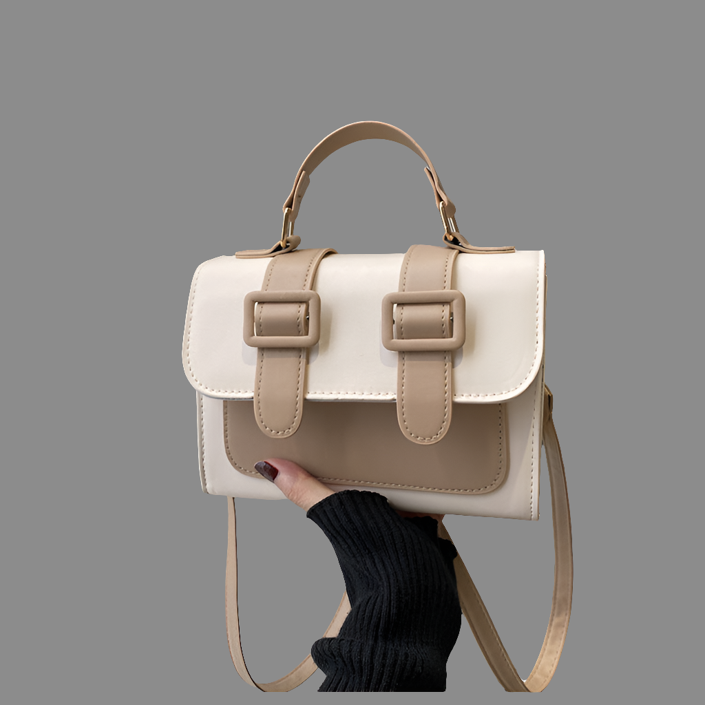 White and beige handbag with a strap held by a person against a gray background