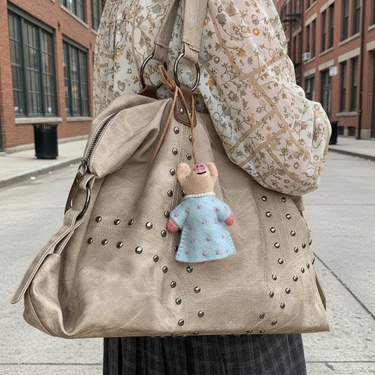 Studded handbag with a plush toy attached, held by a person wearing a gray hoodie.