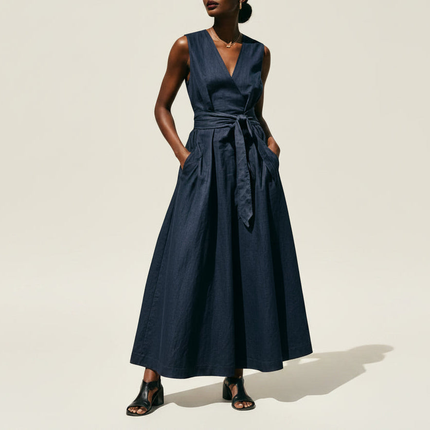 Woman wearing a navy blue sleeveless V-neck maxi dress with a lace-up waist
 on a beige background.