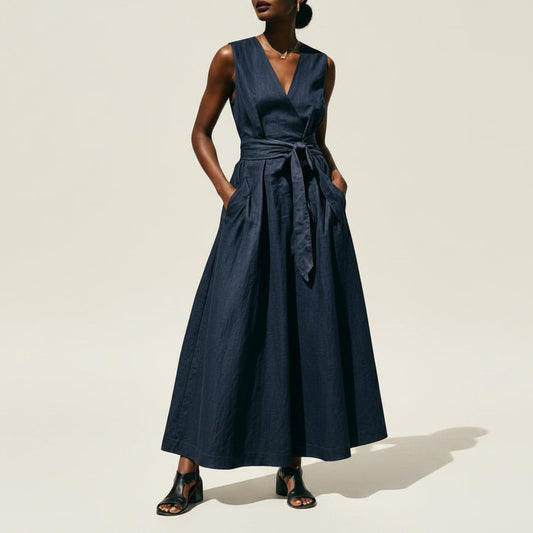 Woman wearing a navy blue sleeveless V-neck maxi dress with a lace-up waist
 on a beige background.
