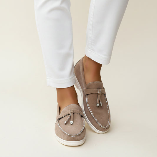 Model wearing taupe women's French tassel loafers styled with black cropped pants