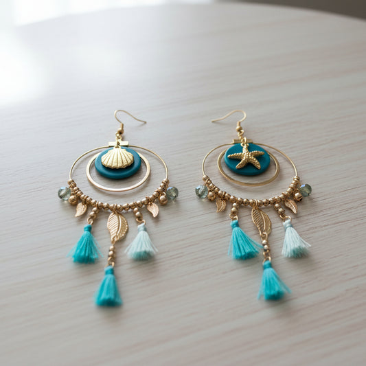 Decorative earrings with blue and gold elements held by a hand against a blurred background