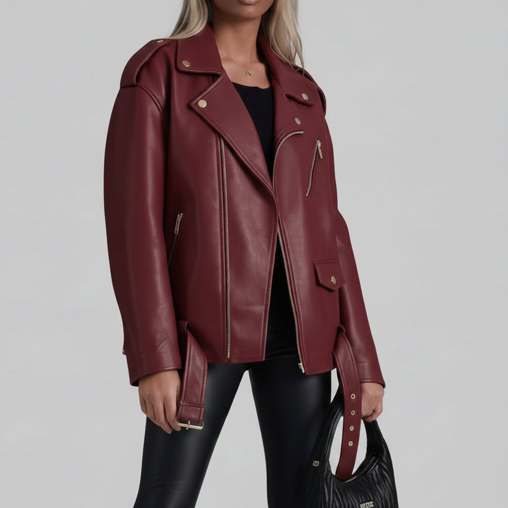 A model wearing a premium oversized dark cherry burgundy faux leather moto biker jacket with silver hardware, styled on a chic outdoor city street.