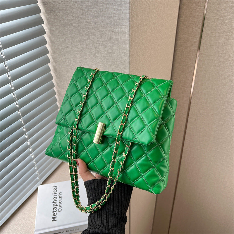 Green quilted messe handbag with gold chain held by a person against a neutral background
